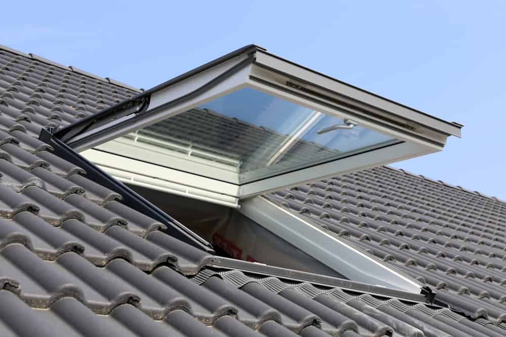 A skylight window is open on a sloped, gray tiled roof under a clear blue sky, allowing light and air into the space below—expertly installed by your trusted roofing contractor Talbot County, MD.