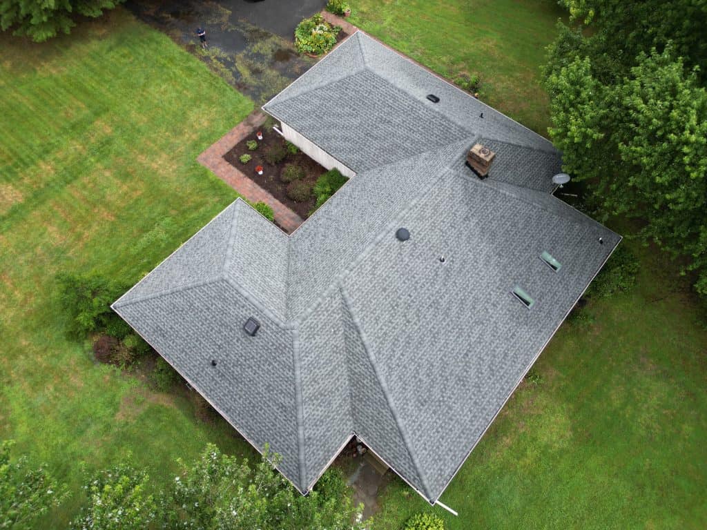 Aerial view of a house with a gray shingled roof, surrounded by green grass, trees, and a brick walkway leading to the front entrance—showcasing the craftsmanship of a top roofing contractor in Talbot County, MD.